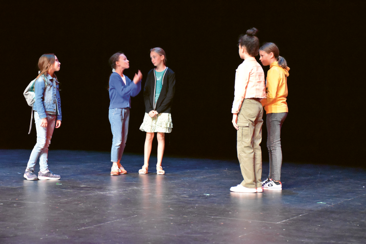 Photo de cinq enfants qui répètent une pièce de théâtre sur scène
