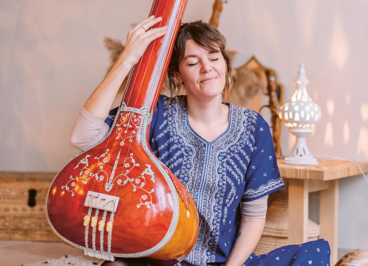 Photo d'une femme assise qui s'appuie contre un instrument de musique indien