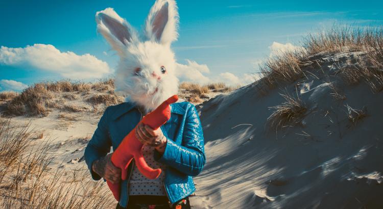 Photo d'une femme portant un masque de lapin et une arme en tissus dans les dunes
